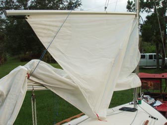 Sail partially raised showing lazy jacks holding main boom and constraining gaff boom and part of sail