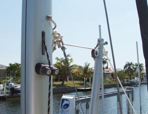 This picture shows the upper end of the MacGregor mast raising pole and the attachment to the mast of the P-23. The line from the winch on the MacGregor pole is led through the block at the tip of the pole and attaches to a ring. Also attached to the same ring are the two stabilizing stays which prevent the mast from swaying. The ring is shackled to a bail through the mast, so the one shackle connects the two baby stays and the mast raising line to the mast bail all at once.