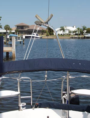 This picture shows a small dinghy engine hoisting davit installed in the stern of the Precision 23, serving double duty as a mast crutch. To serve as a mast crutch, it has a metal V covered by a piece of hose on a custom support which is lashed to the tip of the davit by a few hose clamps. It is also in a good position to use for lifting the outboard engine off the transom bracket, and could be used for its intended purpose as a dinghy engine davit as well. This arrangement serves well for lowering the mast to go under a bridge, but for single hand trailering a much better solution would be to mount a roller on a mast crutch. The dinghy engine davit is an innovative solution, but an easier method would be a simple pole which can be set into a spare set of rudder pintles and gudgeons mounted alongside the ones in use on the rudder. The small offset from the centerline of the boat can be corrected by mounting the roller off center on the pole.